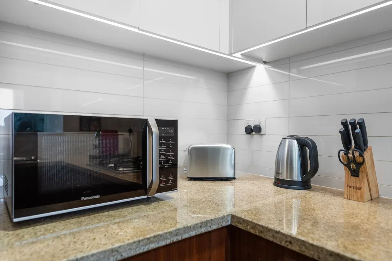 Una encimera de cocina luminosa tiene un microondas, una tostadora, un hervidor y un bloque de cuchillos.