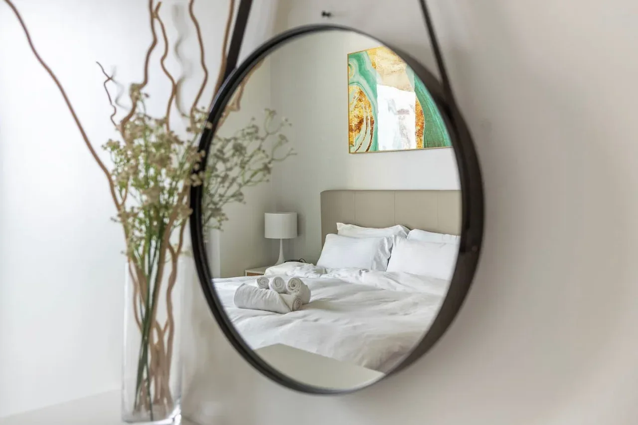 Un dormitorio se refleja en un espejo redondo, con una cama arreglada y arte en la pared.