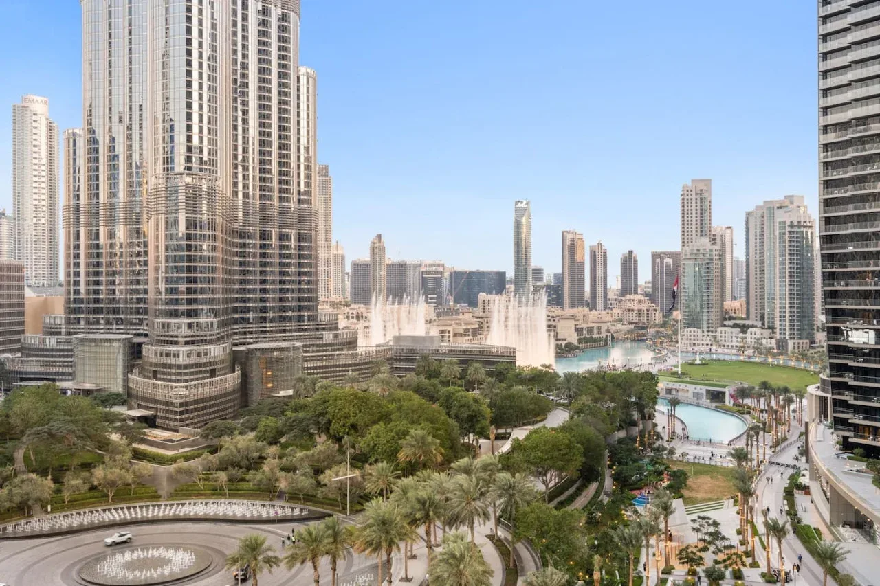 El horizonte urbano domina un parque ajardinado con fuentes y una piscina.
