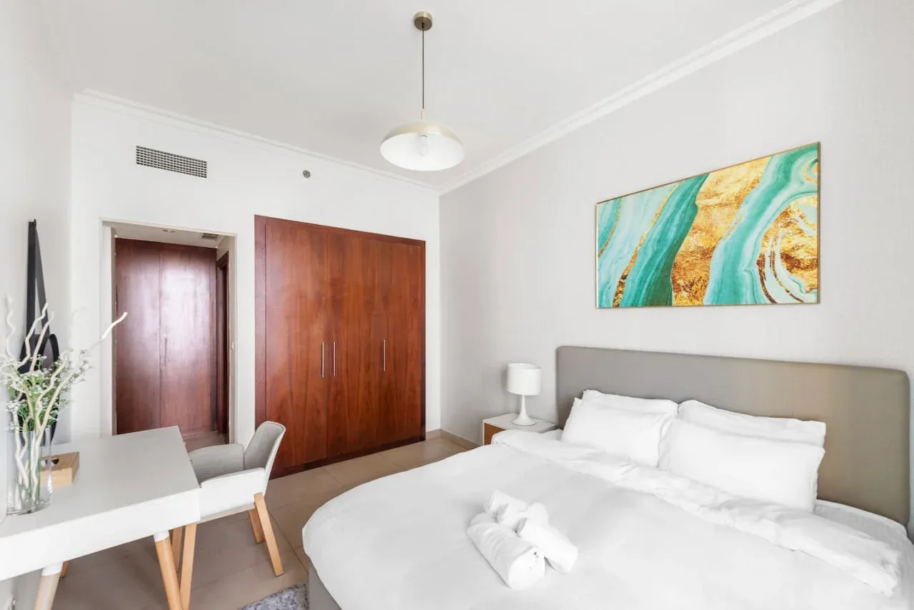 Un dormitorio luminoso con una cama grande y una colorida obra abstracta en la pared.