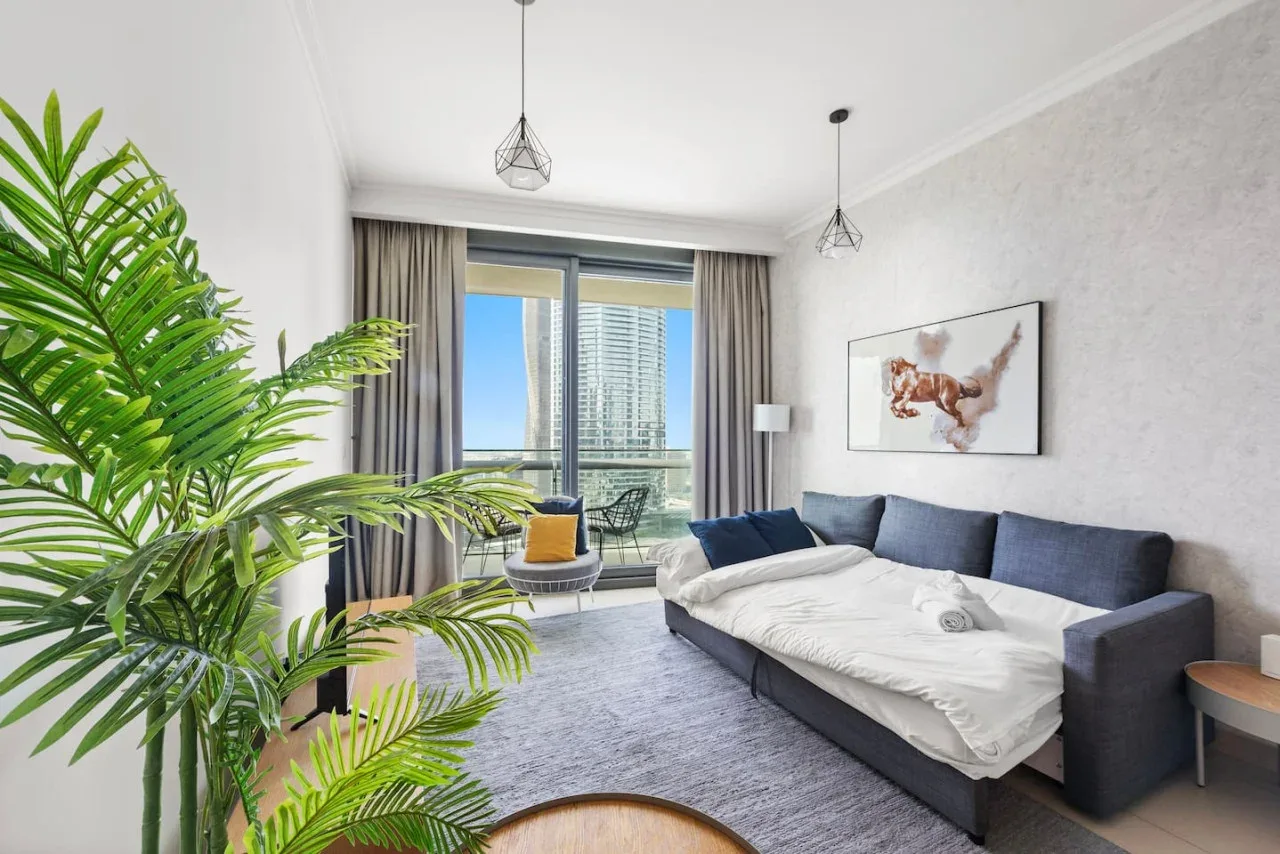 Una sala luminosa con un sofá azul, una ventana grande y una planta frondosa.