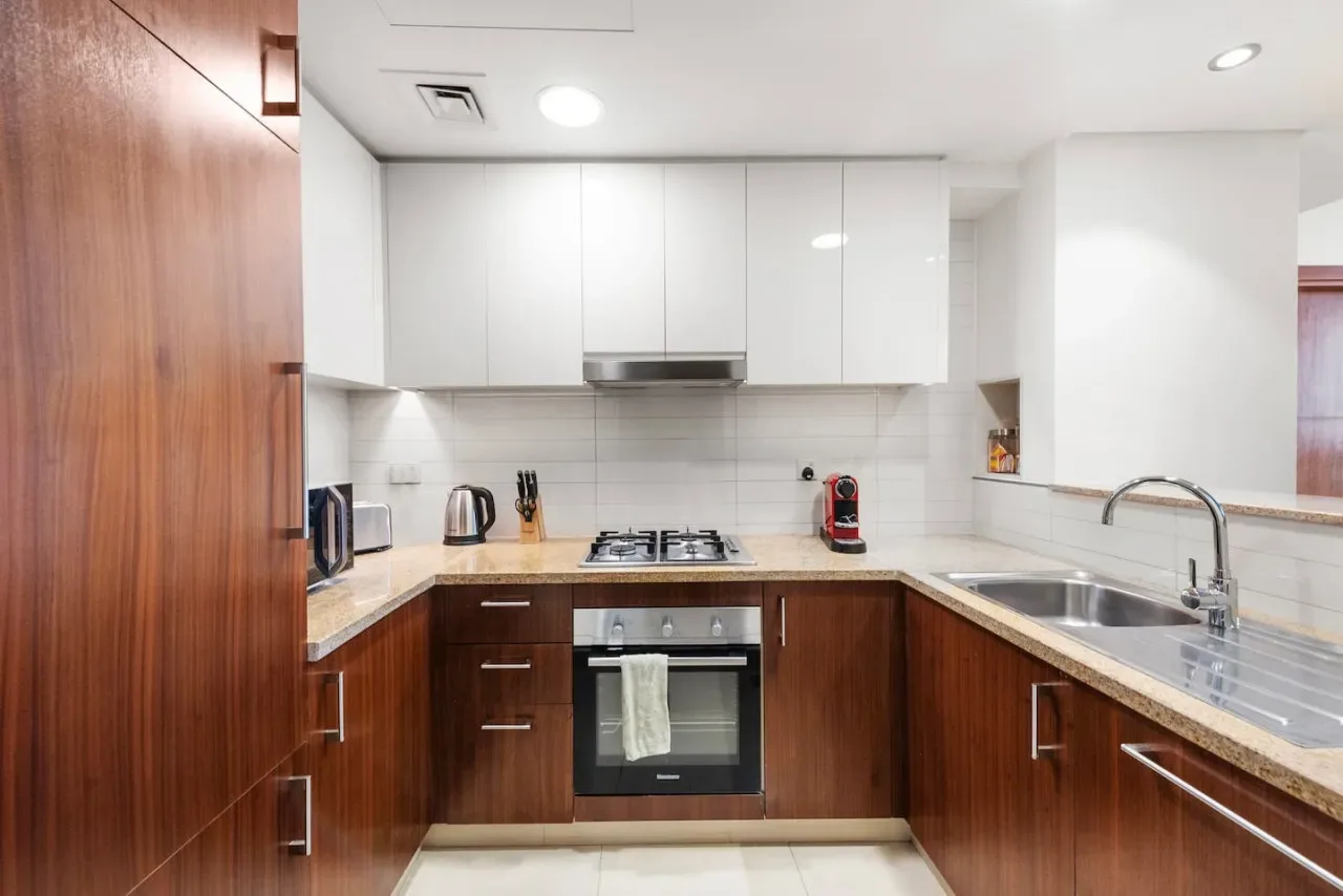 Una cocina moderna con gabinetes de madera, gabinetes superiores blancos y una zona de cocción central.