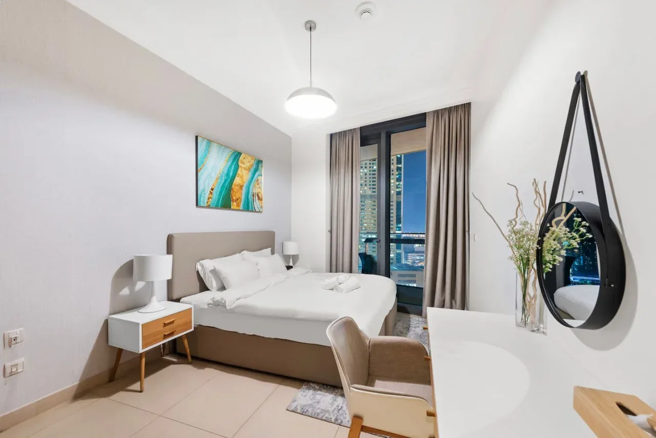 Un dormitorio luminoso con una cama, mesitas de noche y una ventana grande.