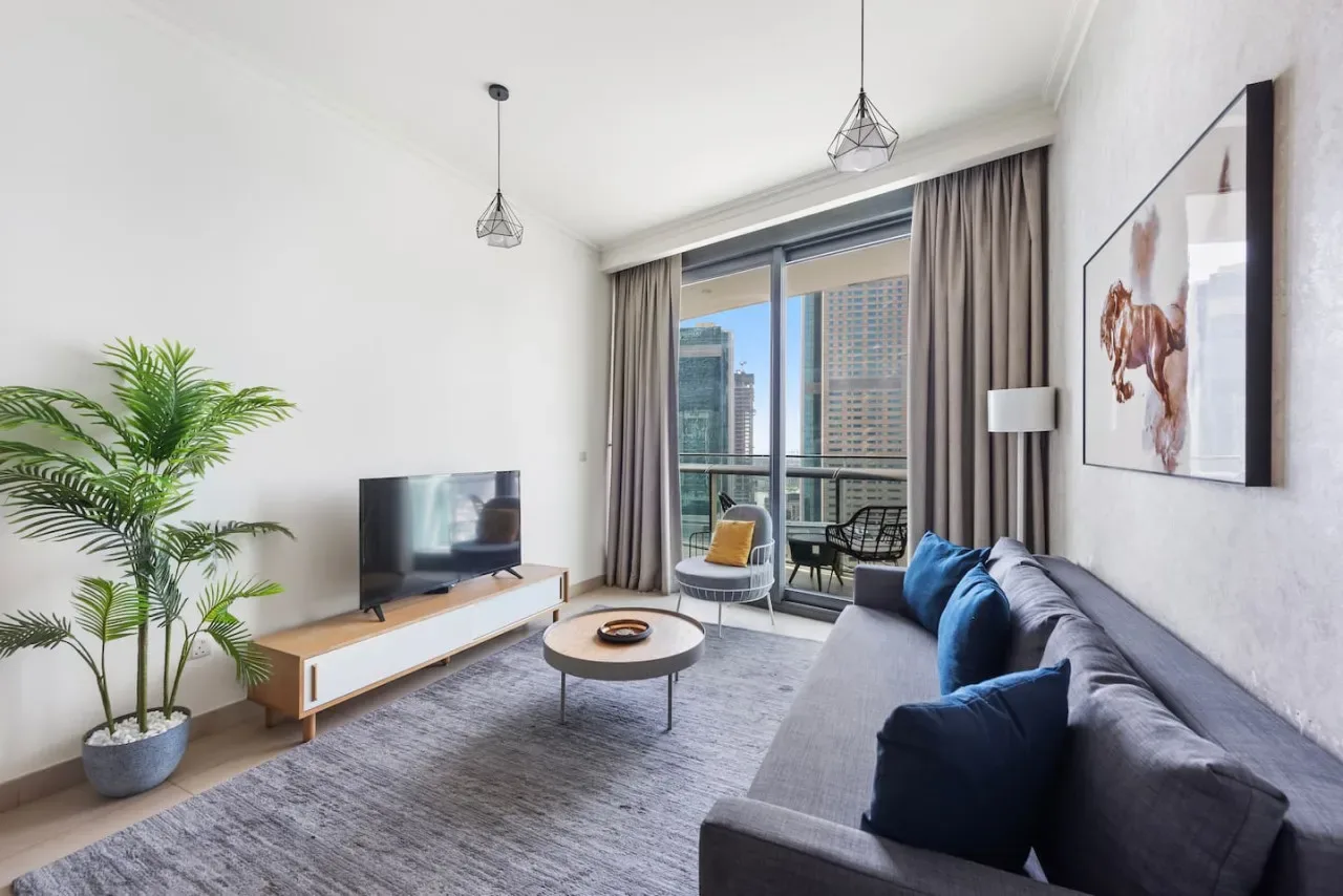 Una sala luminosa con una zona de estar y grandes ventanas con vistas a edificios de la ciudad.