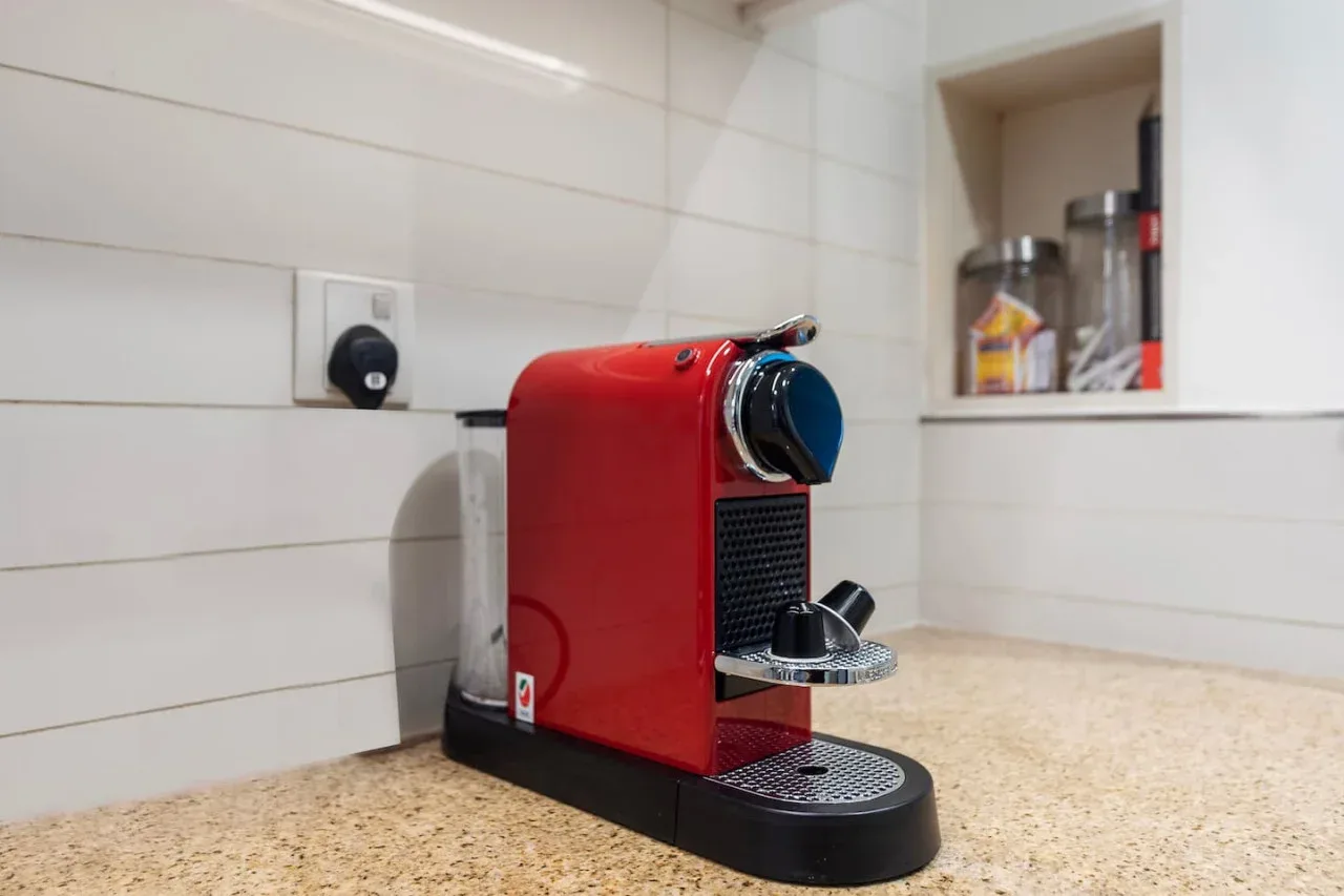 Una cafetera roja está sobre una encimera de cocina, junto a una pared de azulejos.