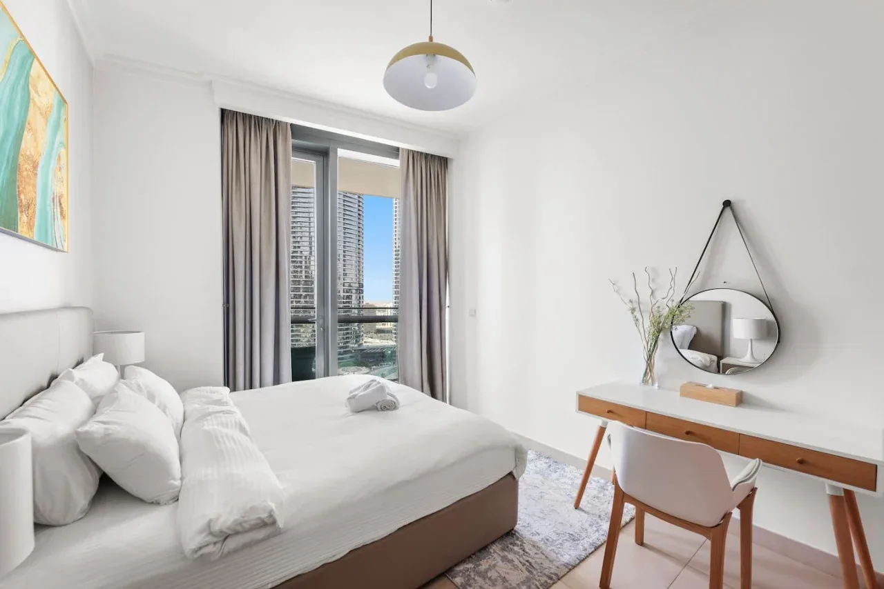Un dormitorio luminoso con una cama junto a un escritorio y una ventana grande.