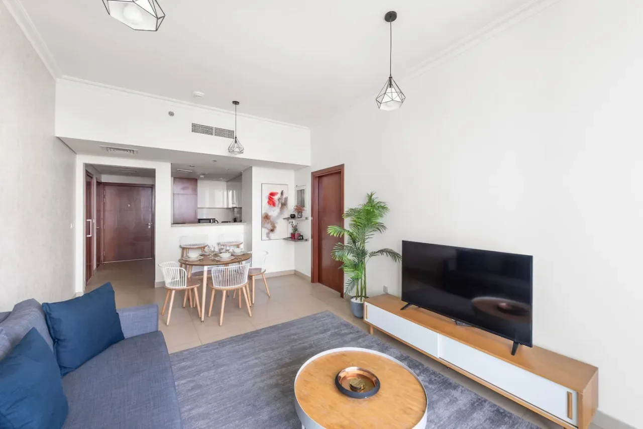 Una sala luminosa con asientos, un televisor y una cocina abierta.