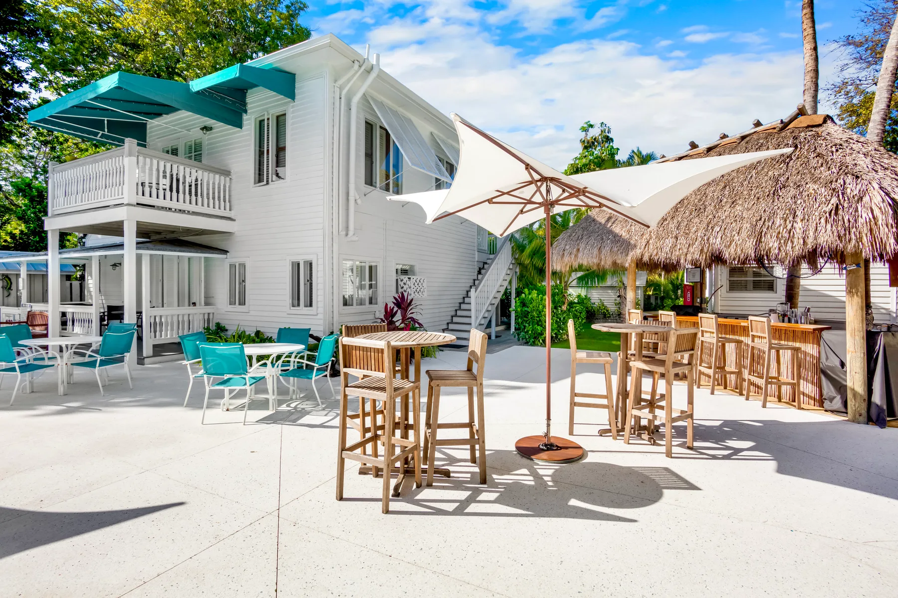 Outdoor patio with tables, umbrellas, and chairs beside the hotel and thatched-roof bar