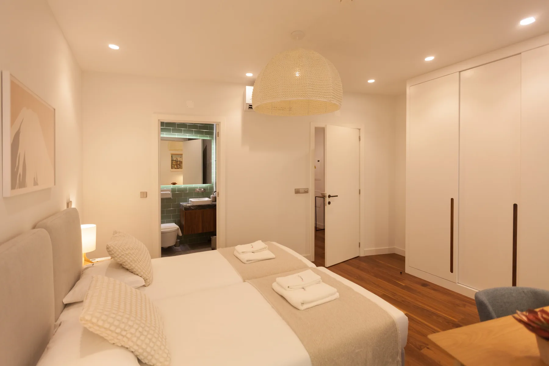 A bedroom with a neatly made bed, bedside lighting, and built-in wardrobes.