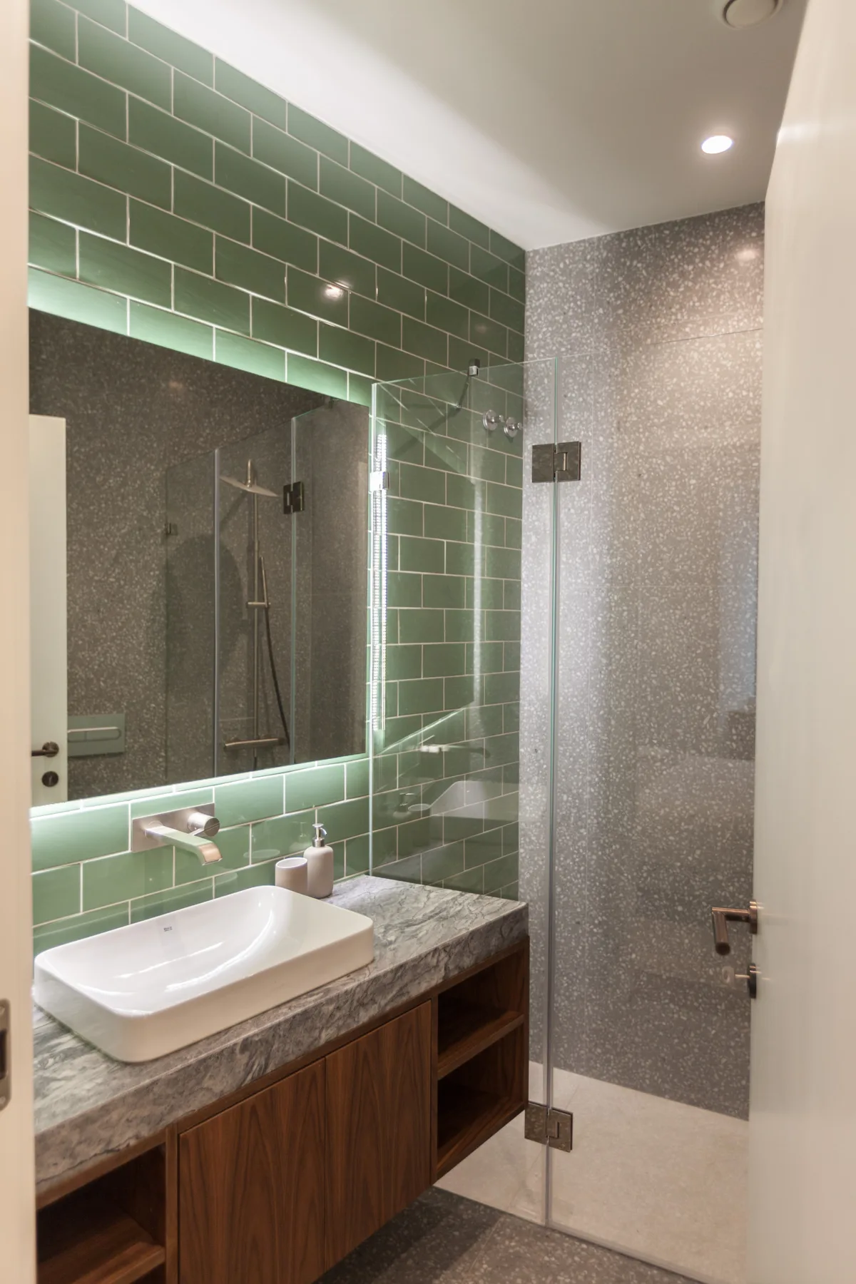 A bathroom with a green-tiled wall, sink, and glass shower.