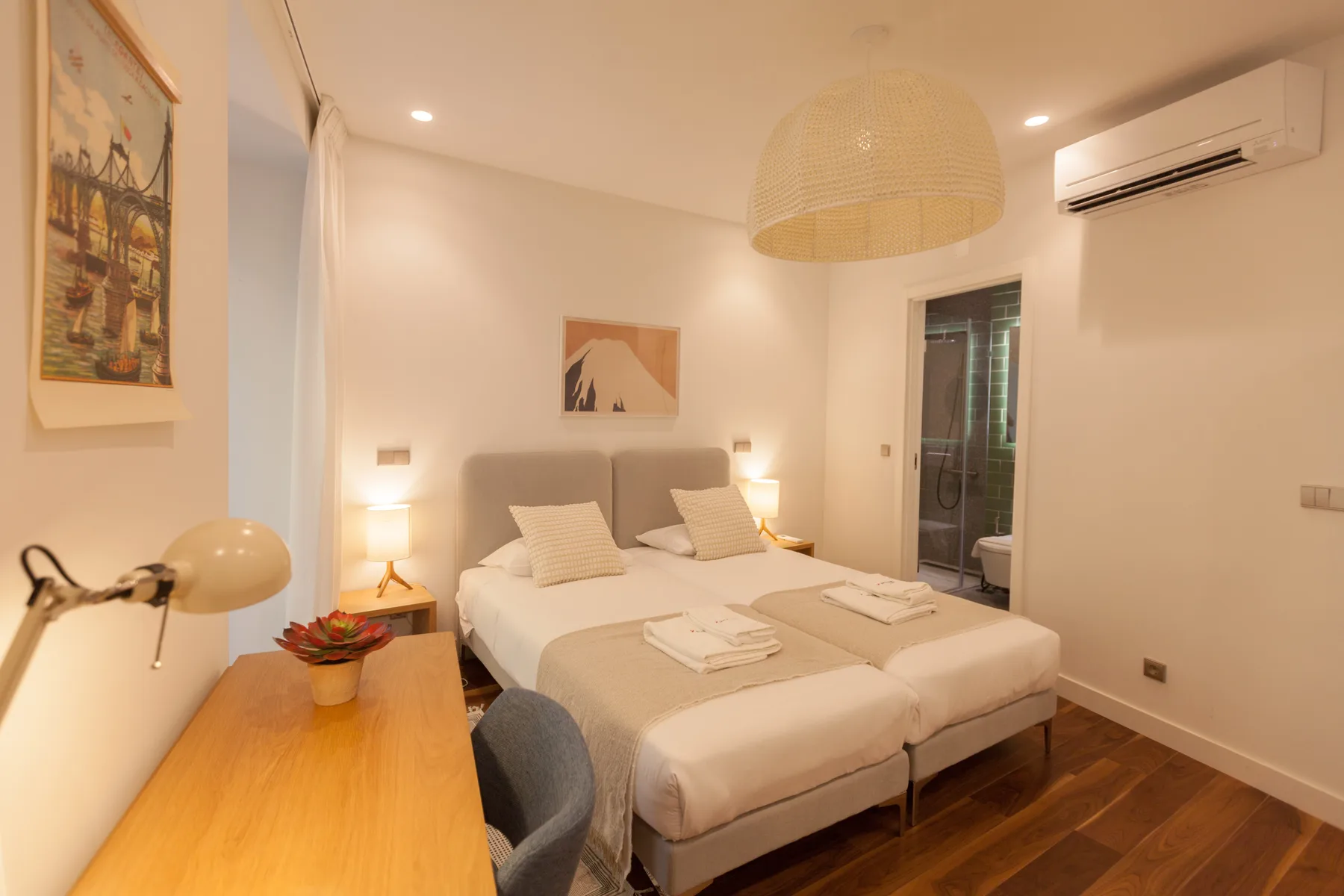 A bedroom with two beds, bedside tables, and a desk.