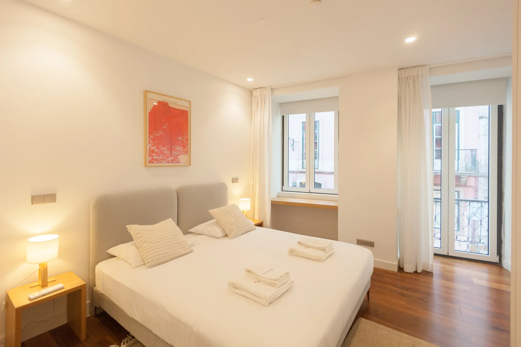 A bedroom with a double bed, bedside table, and tall windows.