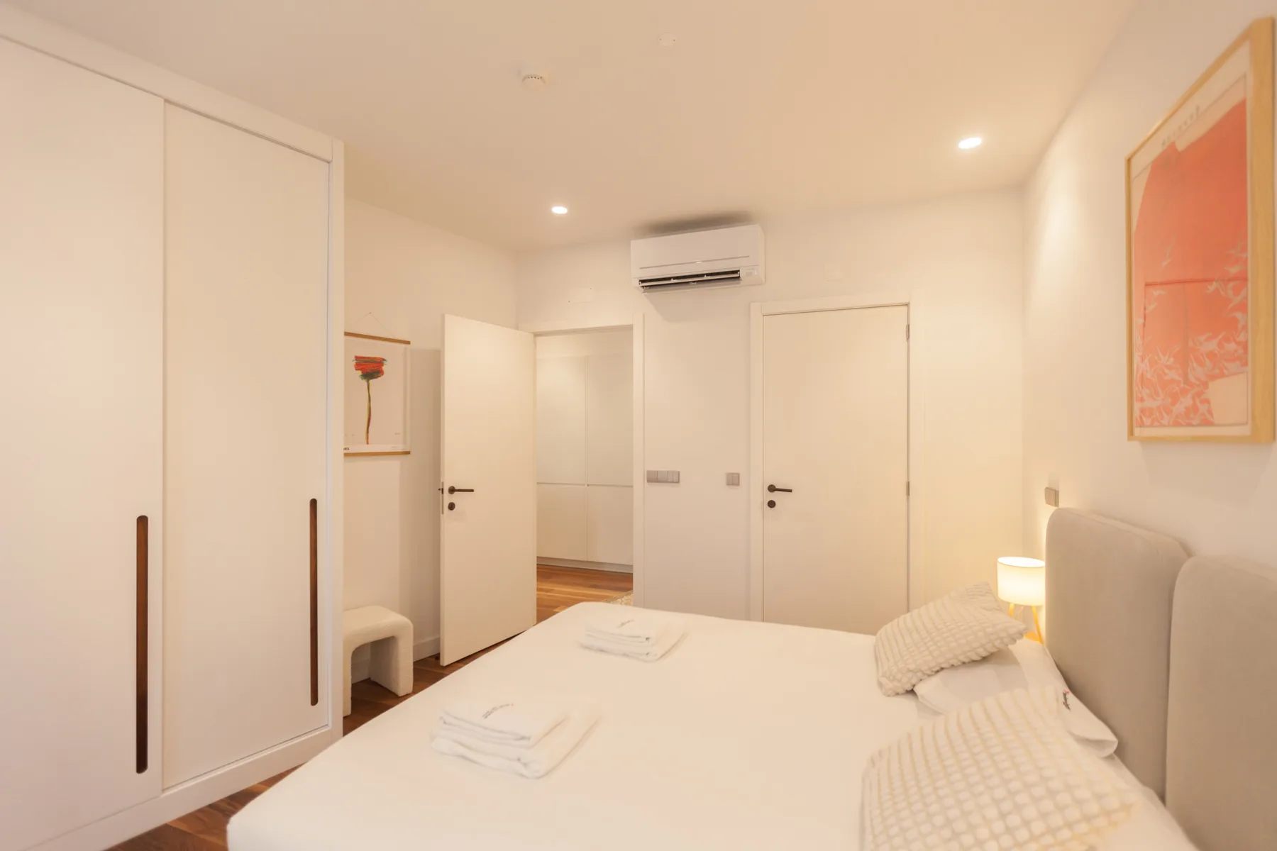 A bright bedroom with a bed, built-in wardrobes, and an air conditioner.