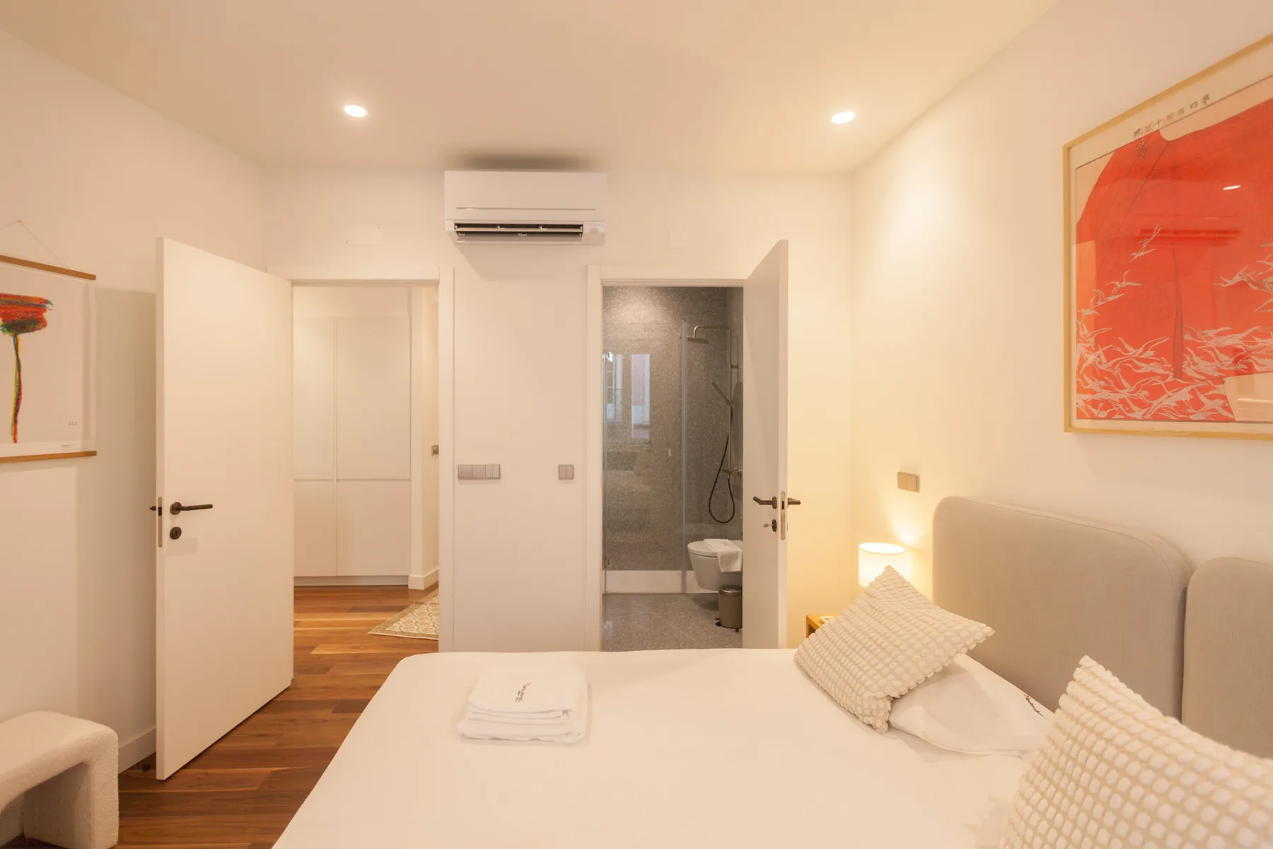 A bright bedroom with a bed and an open doorway to the bathroom.