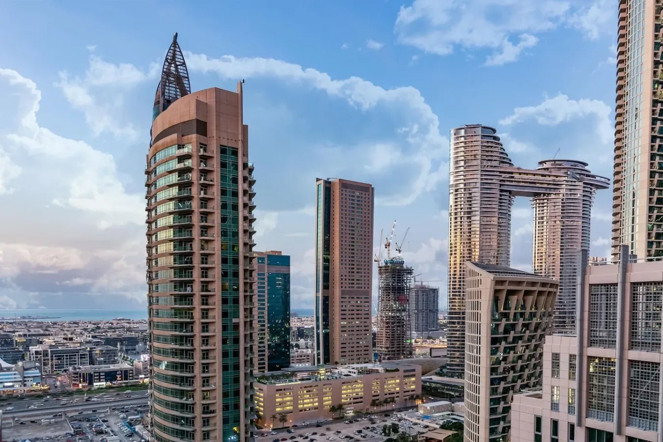 A city skyline with modern high-rise buildings beneath a partly cloudy sky.