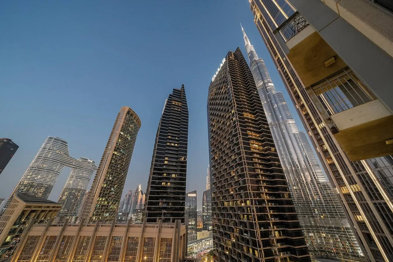 A city skyline of tall modern buildings rises against a clear blue sky.
