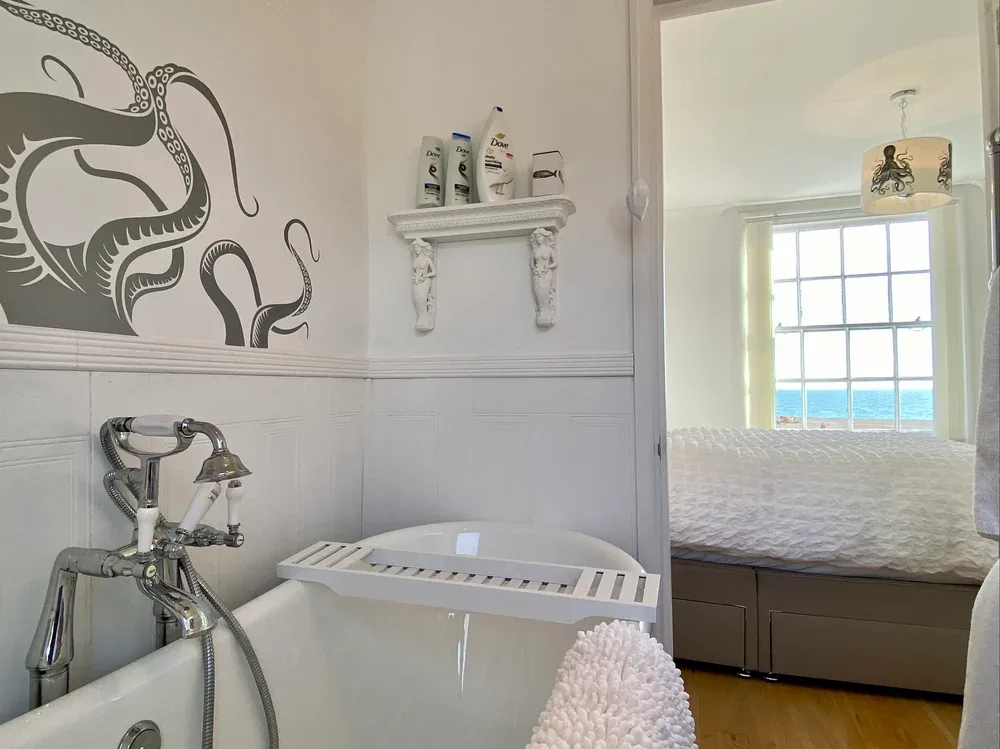 A bathroom with a bathtub beside a bedroom with a window overlooking the water.