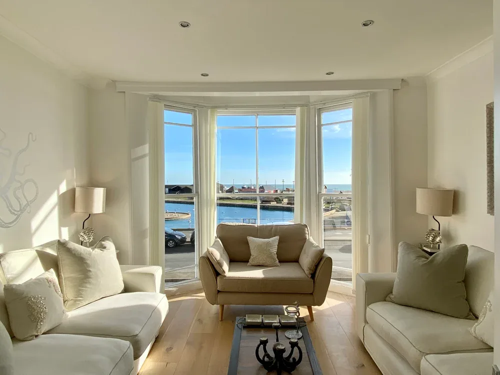 A bright living room with seating arranged around a coffee table and large windows.
