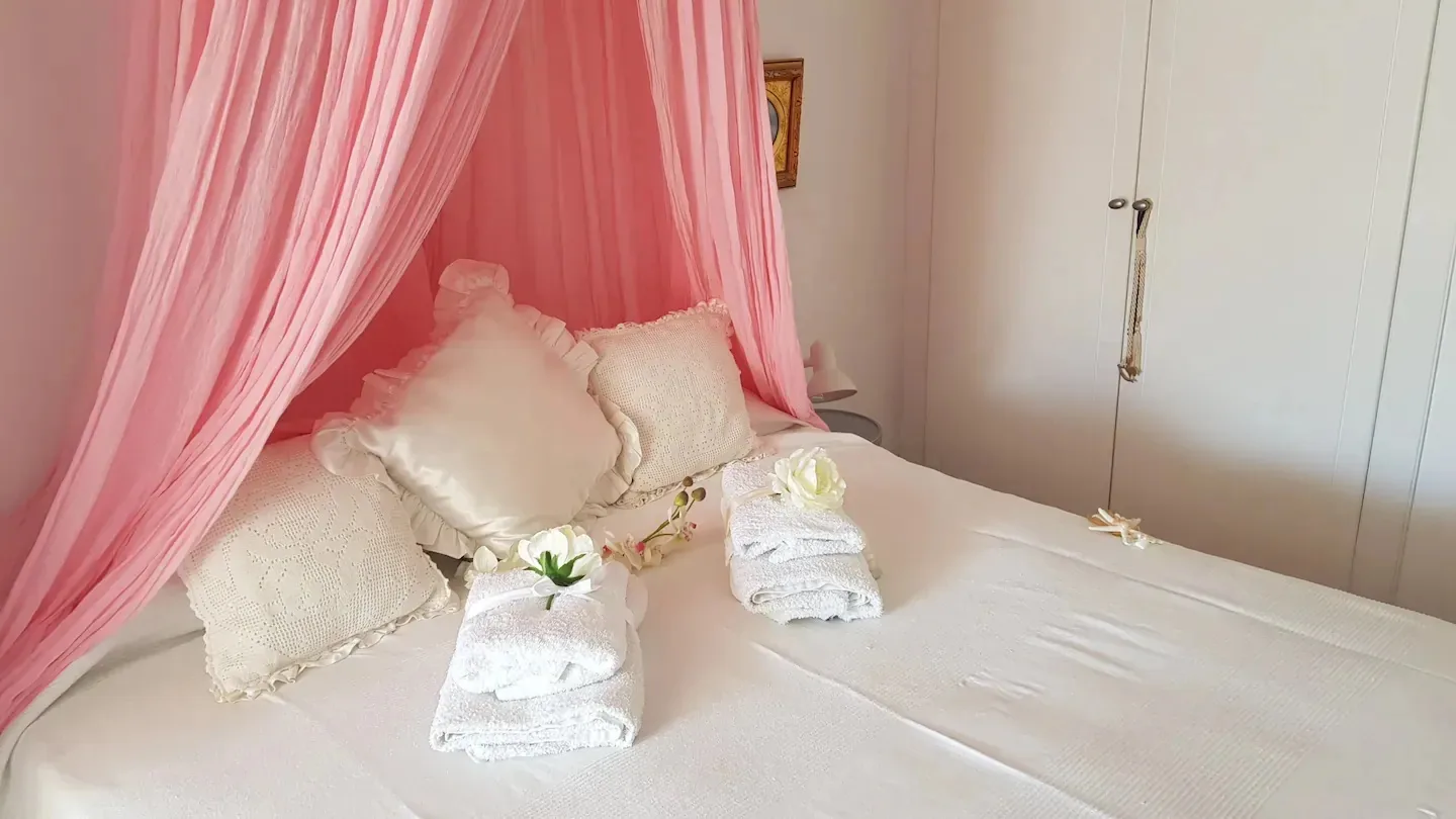 Un dormitorio con una cama vestida con sábanas blancas bajo una tela rosa drapeada.