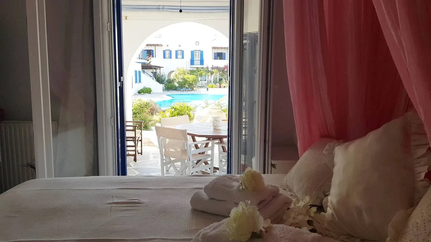 Un dormitorio da a un patio soleado con asientos y vegetación.