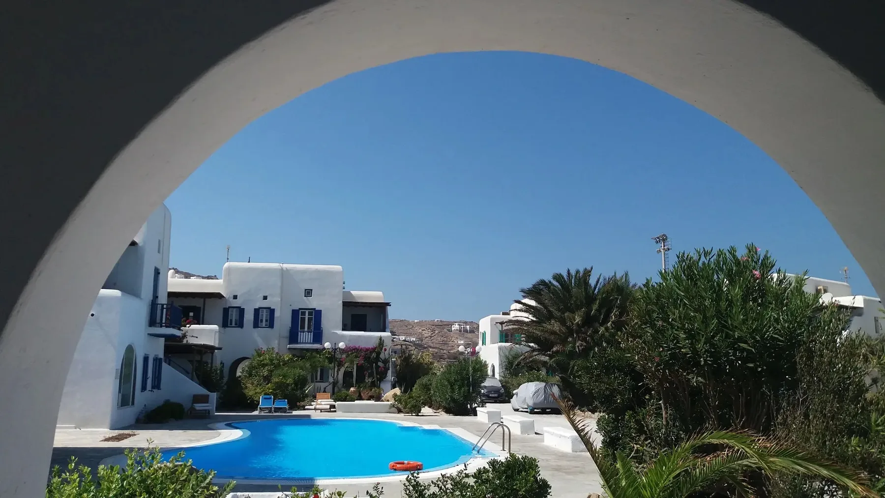 Una piscina y edificios cercanos se ven a través de un arco blanco.
