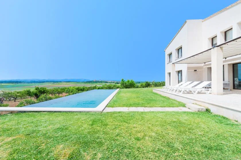 Una casa blanca moderna da a una piscina y un césped verde.