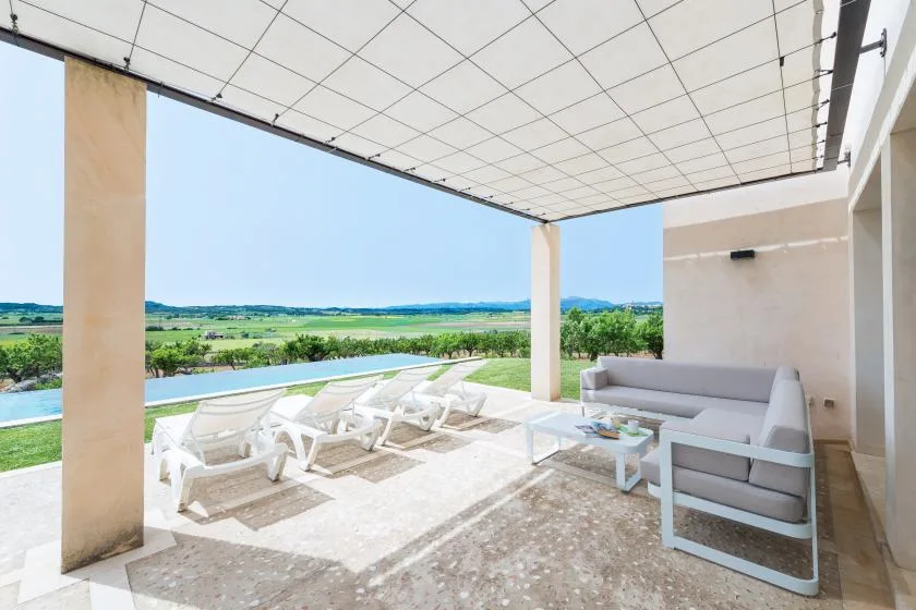 Un patio cubierto con asientos al aire libre da a campos verdes y colinas lejanas.