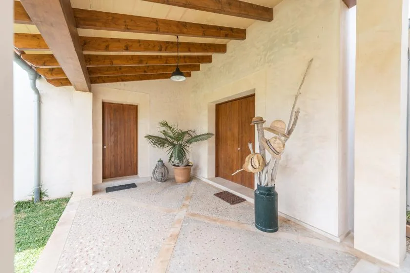 Una entrada cubierta con puertas de madera, vigas expuestas y una planta en maceta.