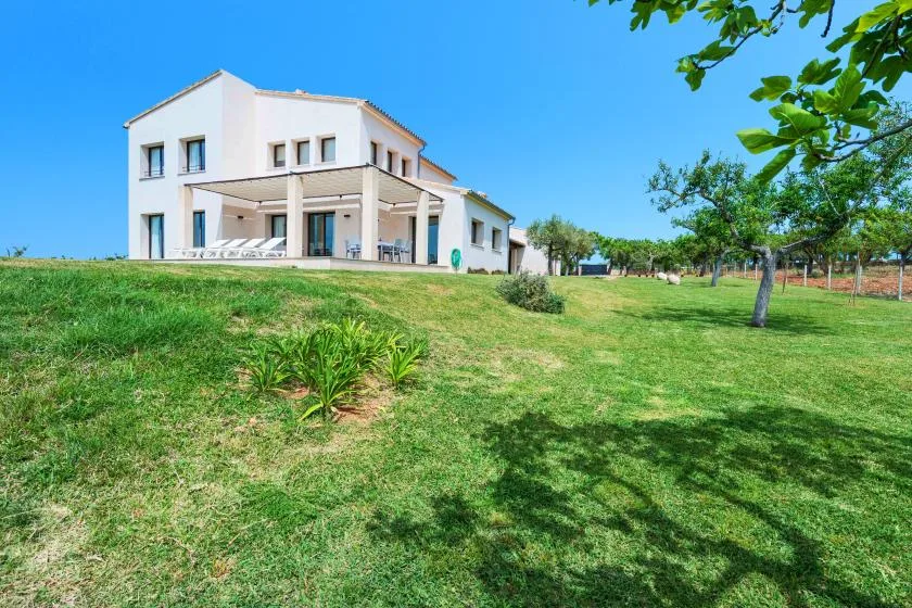 Una casa blanca moderna se alza junto a un amplio césped verde bajo un cielo despejado.