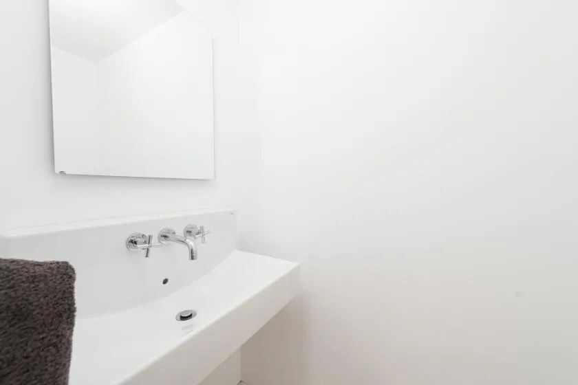 Un lavabo blanco con grifo de pared y espejo.