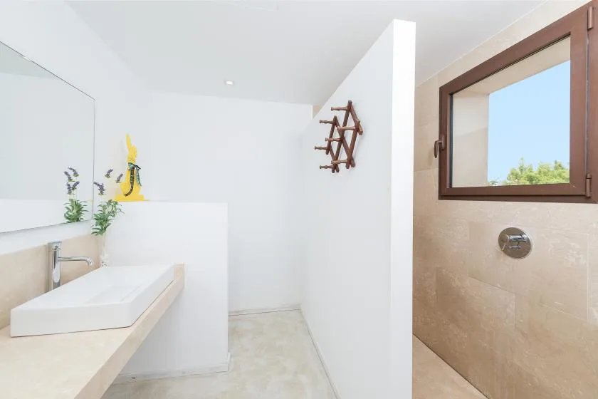 Un baño luminoso con un lavabo y una ventana sobre la zona de ducha.
