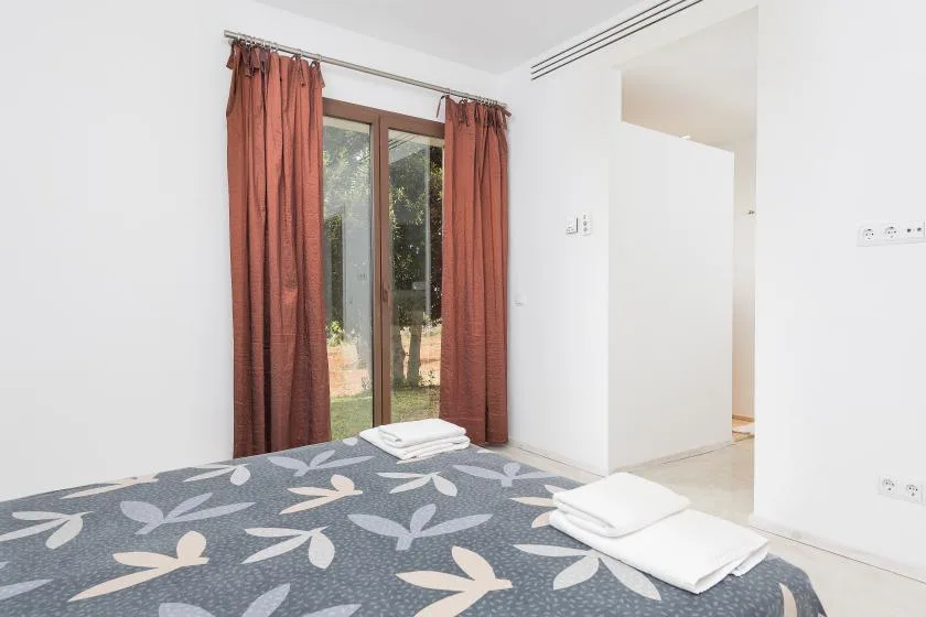 Un dormitorio con una colcha estampada y puertas de vidrio enmarcadas por cortinas.