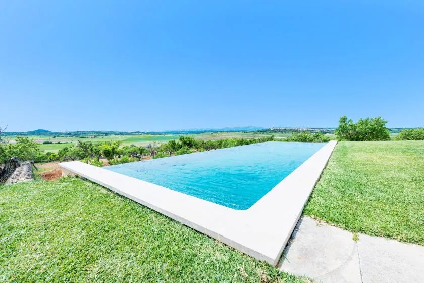 Una piscina está rodeada de césped, con campo abierto al fondo.