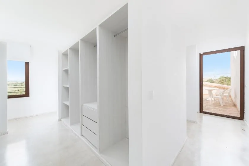 Una habitación blanca y luminosa con estantes abiertos y una puerta de vidrio al patio.