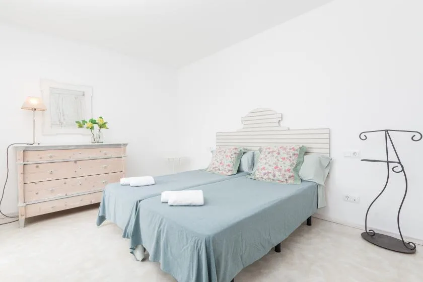 Un dormitorio luminoso con una cama vestida con ropa de cama azul claro y una cómoda de madera.