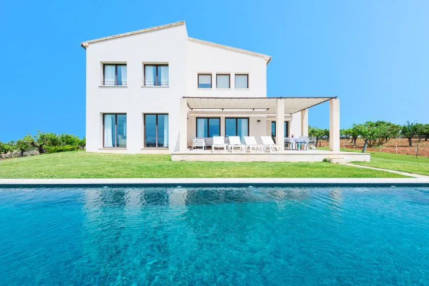 Una casa blanca moderna se encuentra junto a una piscina bajo un cielo despejado.