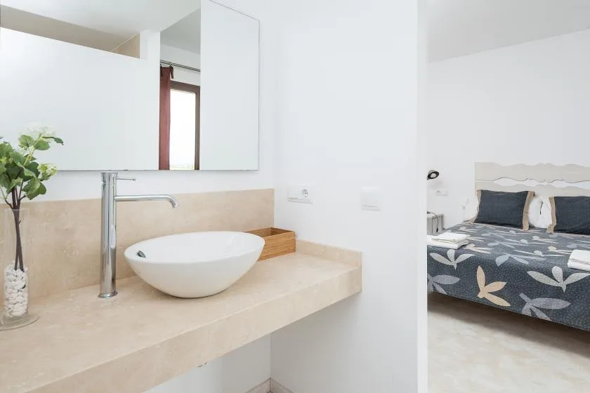 Un lavabo de baño luminoso con un lavabo sobre encimera junto a un dormitorio.