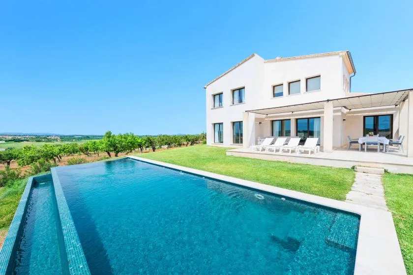 Una casa moderna da a una piscina, con asientos de descanso en el patio.
