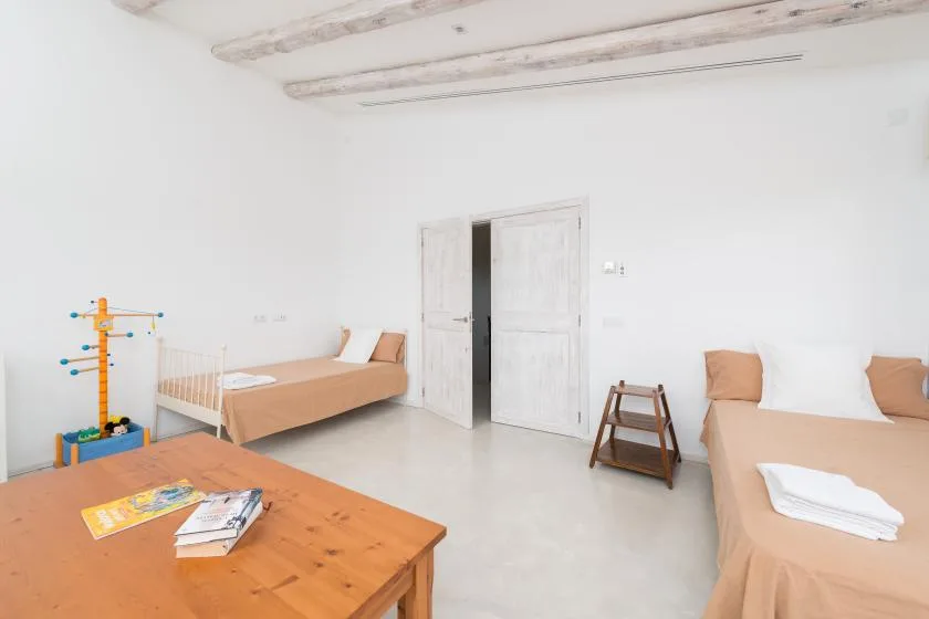 Un dormitorio luminoso con varias camas, una mesa de madera y vigas expuestas en el techo.