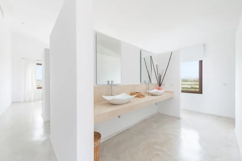 Un baño luminoso con una encimera larga, dos lavabos y un espejo grande.