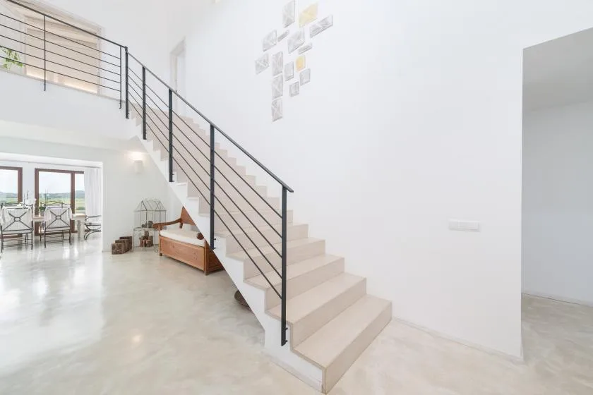Un interior luminoso con una escalera y barandilla negra junto a un comedor.