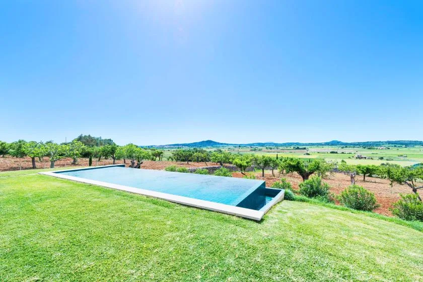 Una piscina al aire libre junto a un césped, con campo abierto al fondo.