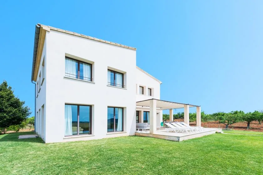 Una casa blanca moderna se alza junto a un césped verde bajo un cielo azul despejado.