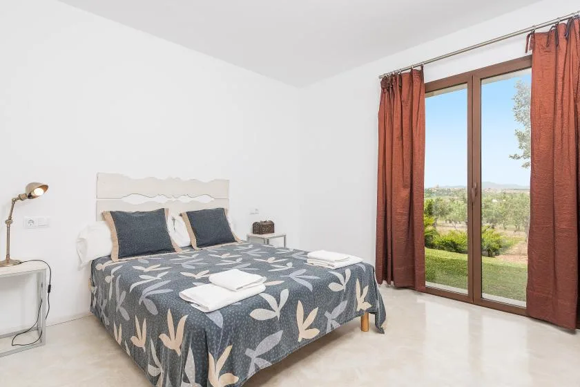 Un dormitorio con una cama doble junto a una gran ventana con cortinas color óxido.