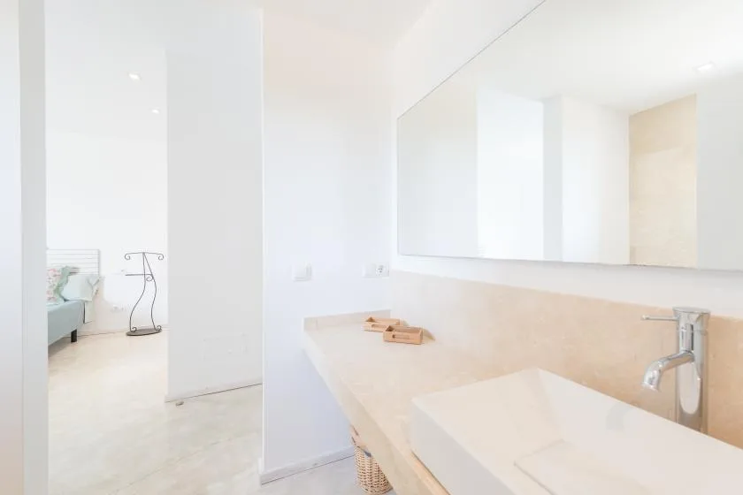 Un baño luminoso tiene un lavabo largo y armarios con espejo.