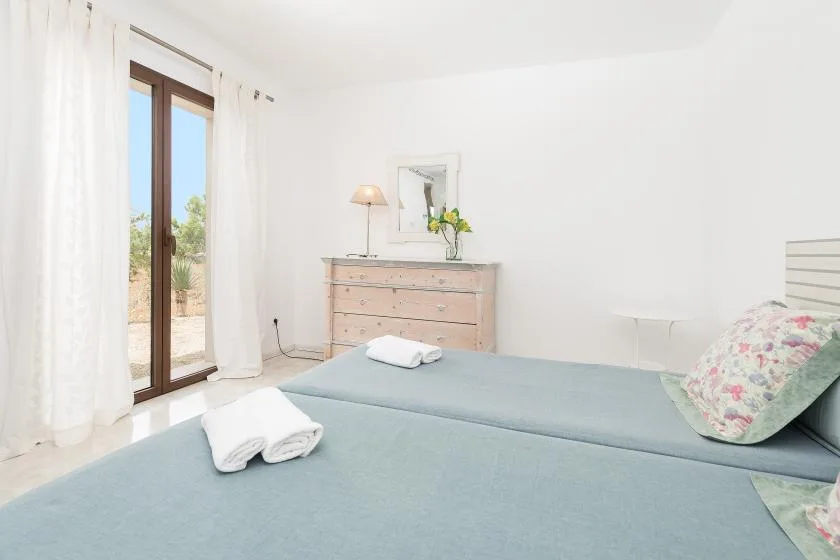 Un dormitorio luminoso con ropa de cama azul y una cómoda junto a la ventana.