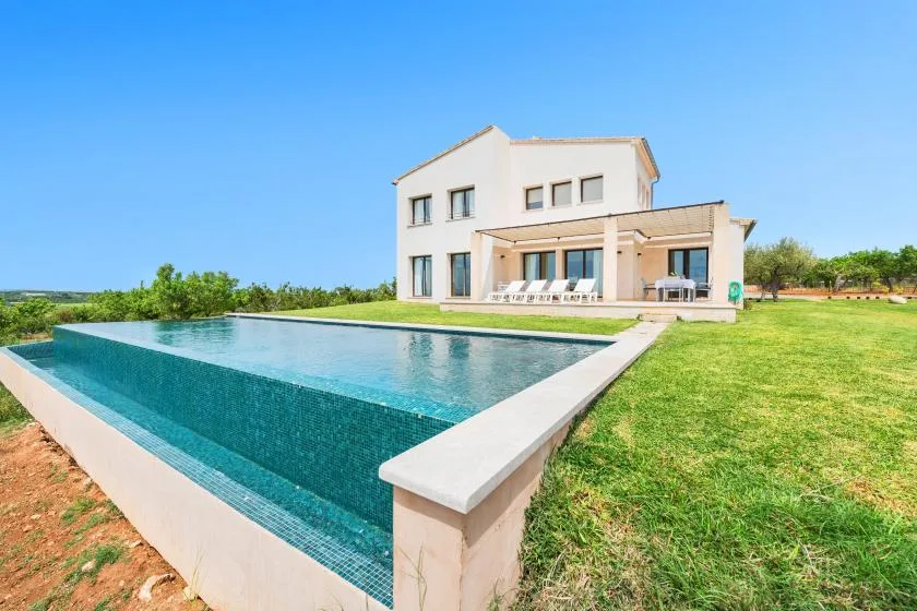 Una casa moderna está junto a una piscina rectangular y un césped.