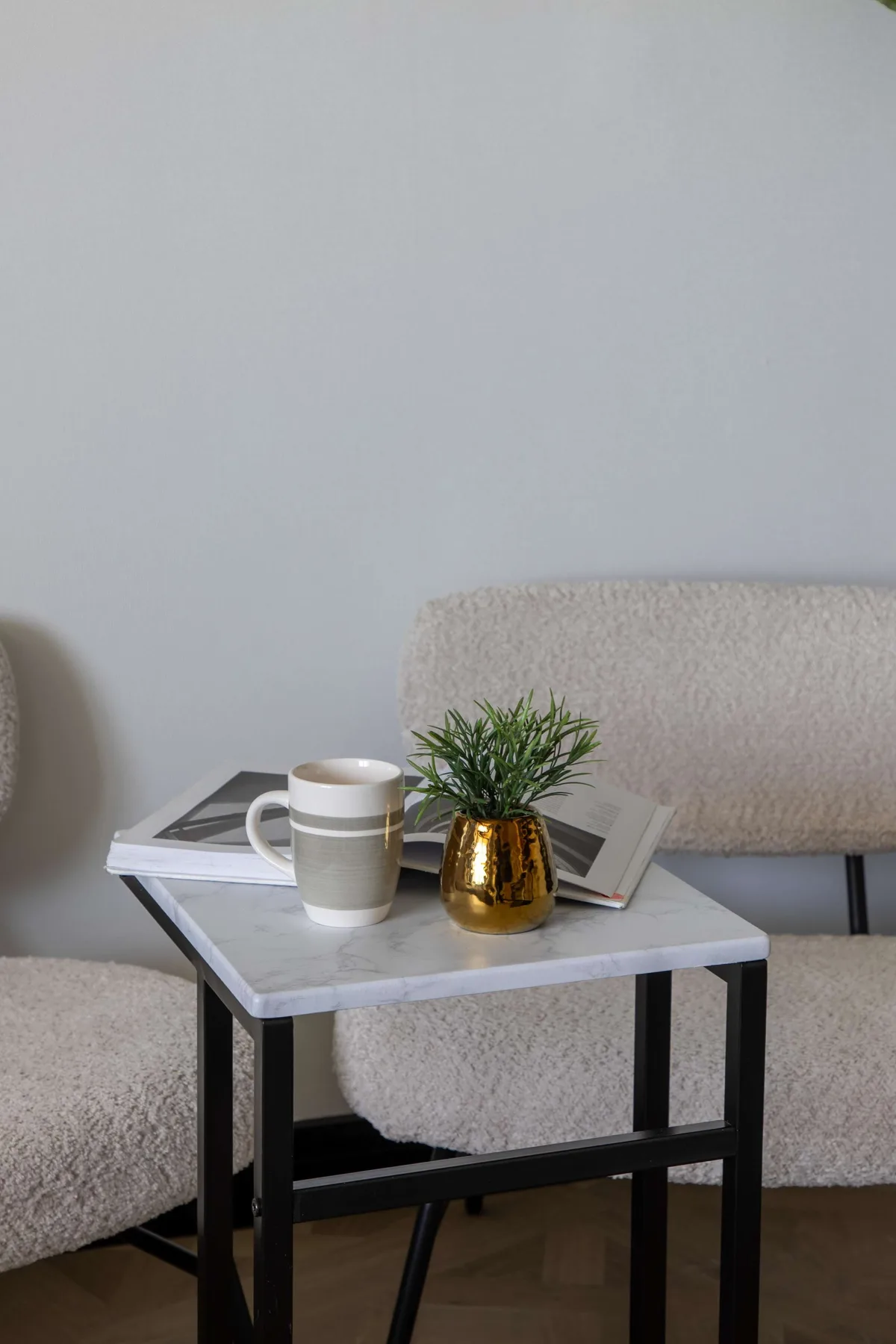 A small table with a mug and plant sits beside upholstered seating.