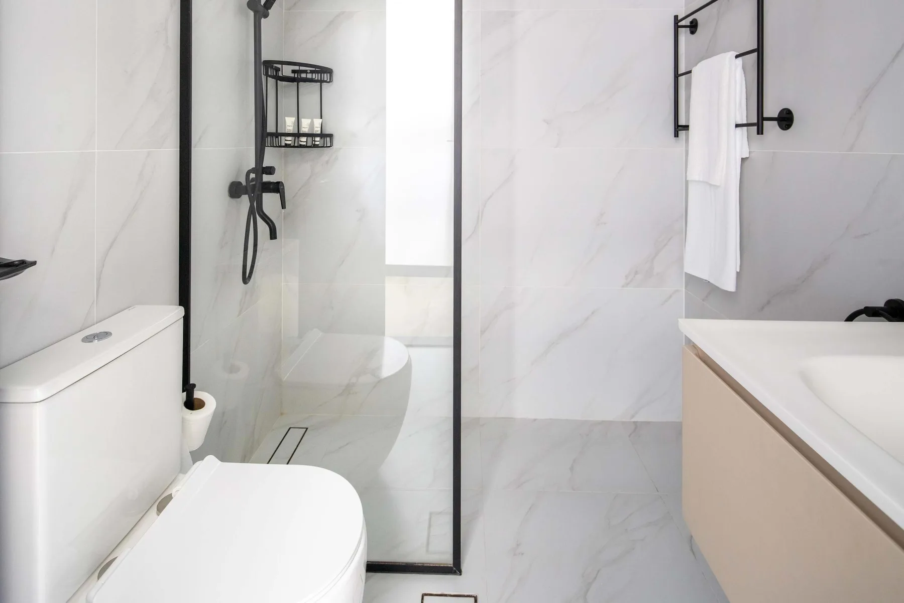 A bright bathroom with a glass shower, toilet, and sink.