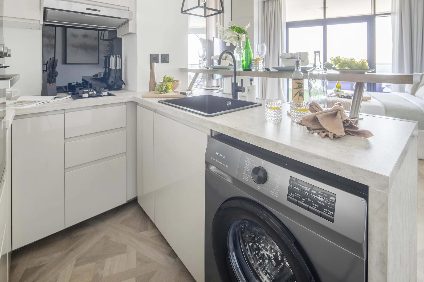 A bright kitchen with a sink, countertop, and front-loading washing machine.